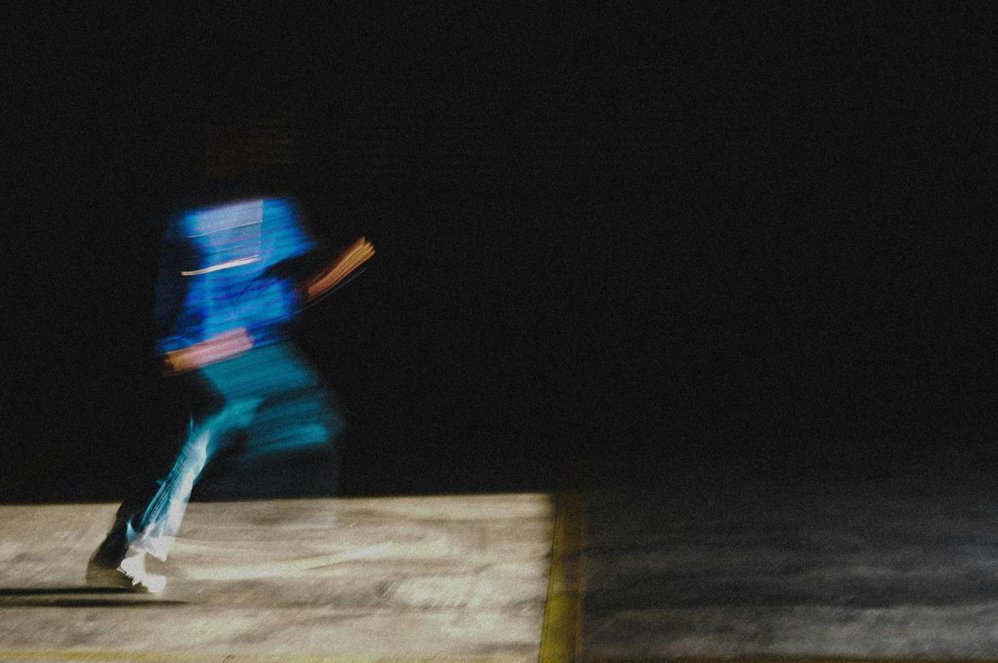 A runner blurred by motion, crossing a dark floor in blue